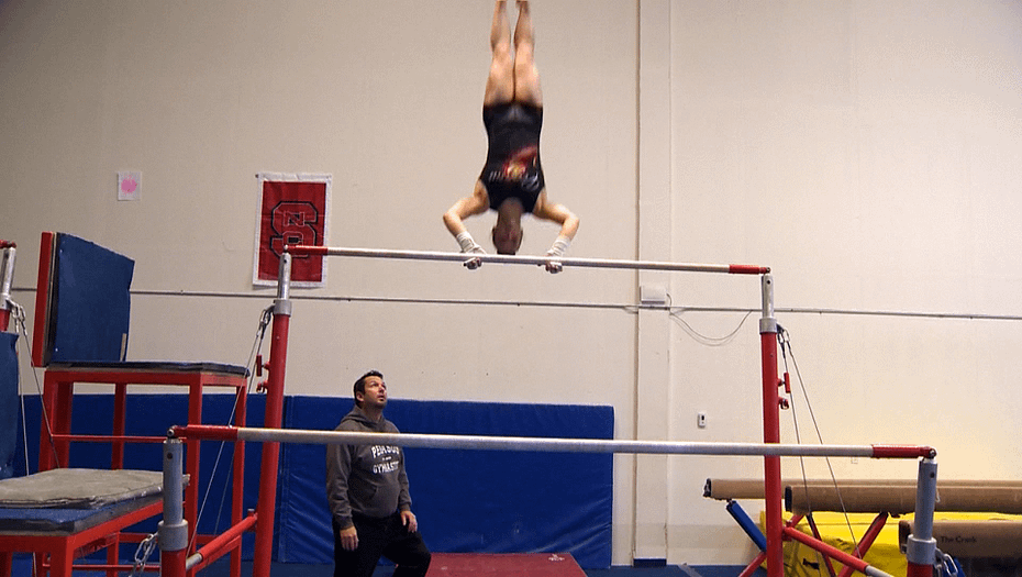 female gymnastics athlete on bars with coach watching
