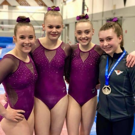 four female gymnastics in club leotards and team jacket